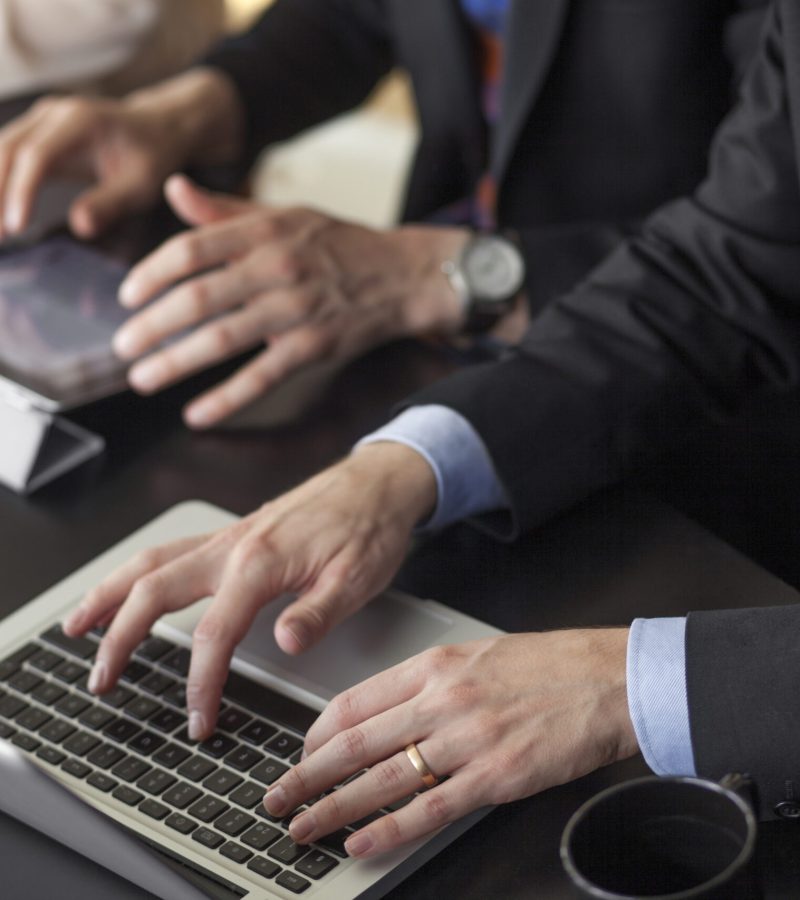 Midsection of business people using laptop and tablet at table in cafe